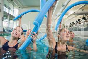Happy fitness class doing aqua aerobics with foam rollers