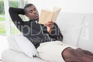 Casual man sitting on his sofa reading a book