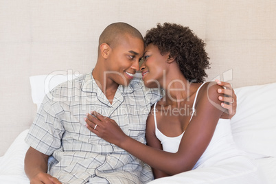 Happy couple sitting on bed cuddling