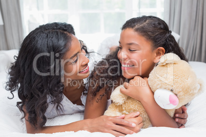 Pretty woman lying on bed with her daughter smiling at each othe