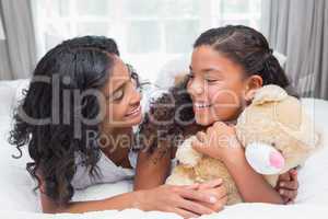 Pretty woman lying on bed with her daughter smiling at each othe