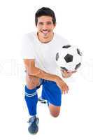 Football player in blue kneeling with ball