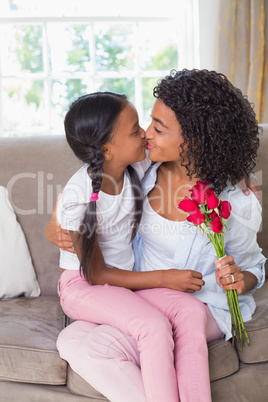 Pretty mother sitting on the couch kissing her daughter holding