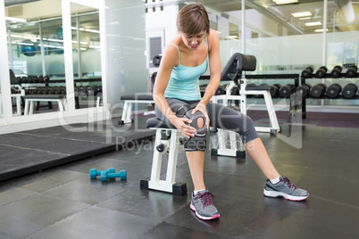 Fit brunette sitting on bench holding injured knee