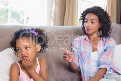 Pretty mother sitting on couch scolding petulant daughter