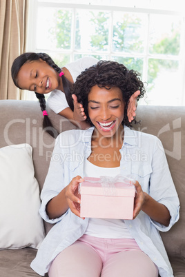 Pretty mother sitting holding gift with her daughter revealing