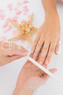 Beautician filing female clients nails at spa beauty salon