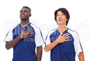 Football players in blue with hands on heart