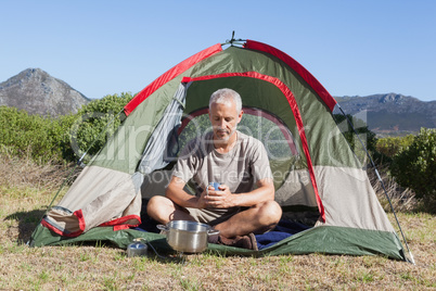 Happy camper holding mug outside his tent