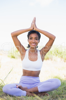 Fit woman sitting on grass in lotus pose smiling at camera