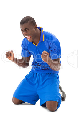 Excited football player in blue cheering on his knees