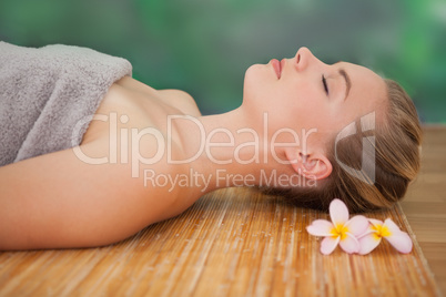 Peaceful blonde lying on bamboo mat with flowers