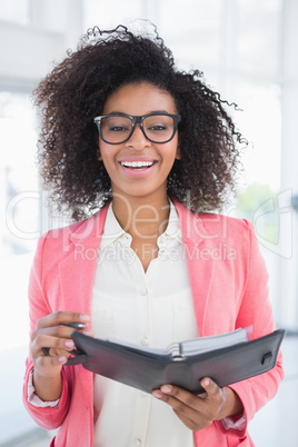 Casual businesswoman holding her diary smiling at camera