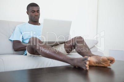 Casual man sitting on sofa using laptop with feet up