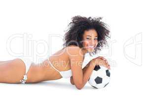 Fit girl in white bikini holding football lying on floor