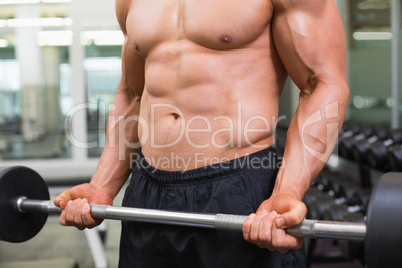 Mid section of a shirtless muscular man lifting barbell