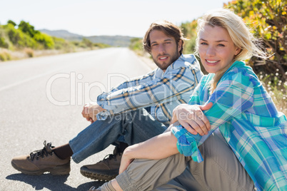 Attractive couple sitting on the road smiling at camera