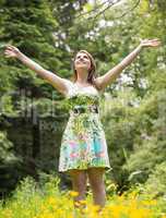 Woman with arms outstretched in field against trees