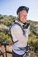 Fit cyclist adjusting helmet strap on country terrain smiling at