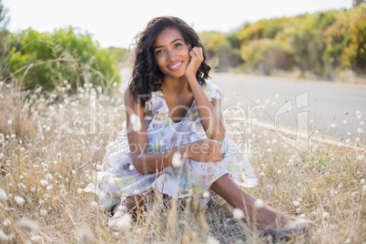 Happy pretty woman sitting on the grass in floral dress