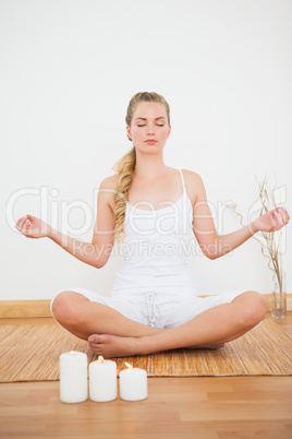 Peaceful blonde sitting in lotus pose on bamboo mat