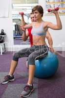 Personal trainer with client lifting dumbbells on exercise ball