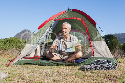 Happy camper looking at map sitting in his tent