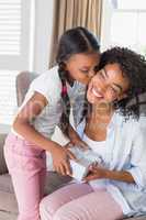 Pretty mother sitting on couch offering daughter a gift