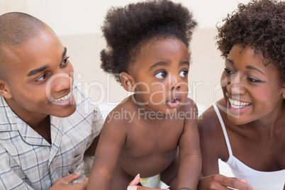 Happy couple sitting on bed with baby daughter