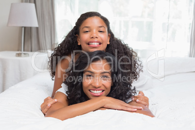 Smiling mother and daughter posing together on bed