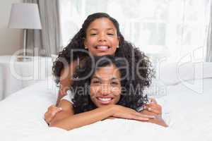 Smiling mother and daughter posing together on bed