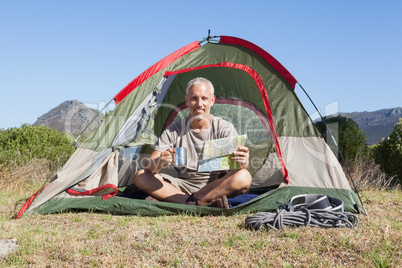 Happy camper looking at map sitting in his tent