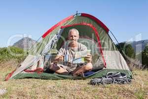 Happy camper looking at map sitting in his tent