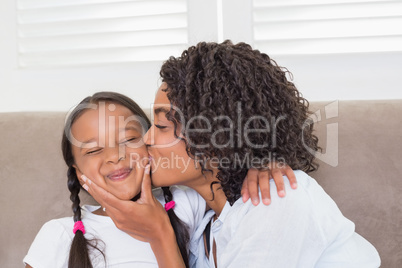 Pretty mother sitting on the couch with her daughter kissing her