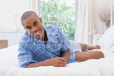 Happy man looking at camera lying on a bed