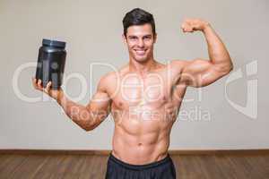 Muscular man posing with nutritional supplement in gym