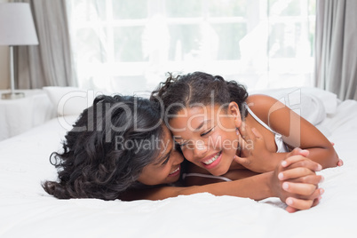 Smiling mother and daughter posing together on bed