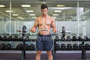 Shirtless muscular man lifting barbell in gym