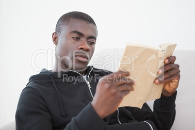 Casual man sitting on his sofa reading a book