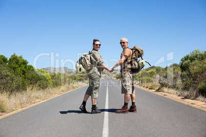 Hitch hiking couple holding hands on the road smiling at camera