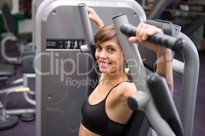 Happy brunette using weights machine for arms