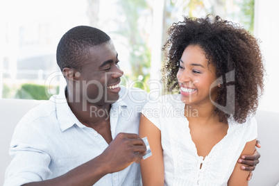 Attractive couple sitting on couch together holding credit card