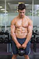 Muscular man lifting kettle bell in gym