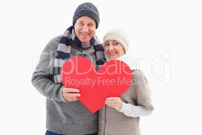 Happy mature couple in winter clothes holding red heart