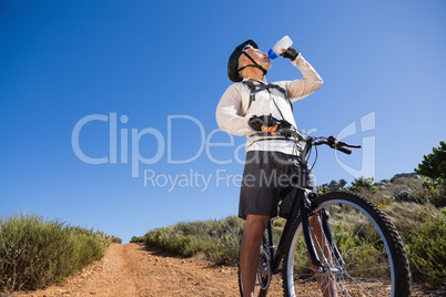 Fit cyclist drinking water on country terrain
