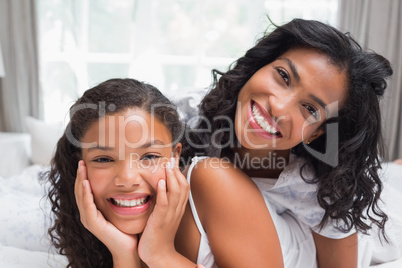 Smiling mother and daughter posing together on bed