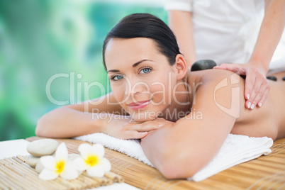 Beautiful brunette enjoying a hot stone massage smiling at camer