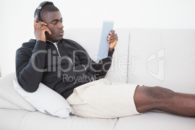 Casual man sitting on his sofa listening to music on tablet pc