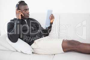 Casual man sitting on his sofa listening to music on tablet pc