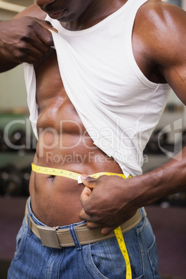 Mid section of a muscular man measuring waist